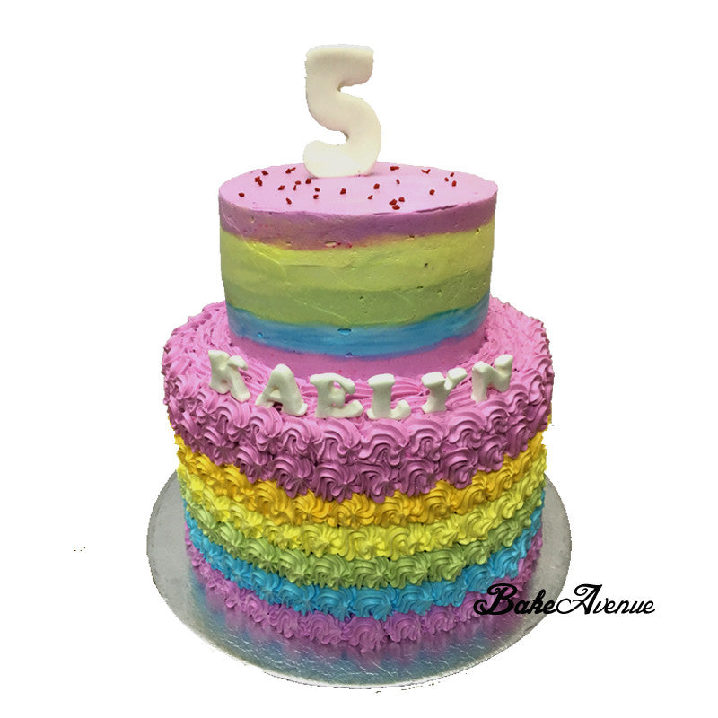 A simple two-tier cake made interesting with a rainbow airbrush pattern and  a striped border and roses made fr…